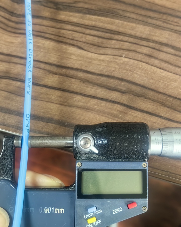 Micrometer measuring the diameter of blue insulated tracer wire